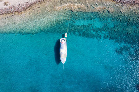 Aerial, top down view to a luxury motor yacht anchored over turquoise water as seen in the Aegean Sea, Greeceの写真素材