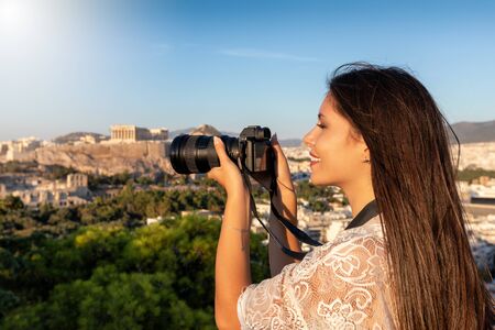 A female Europe traveler takes photographs of the cityscape and Acropolis of Athens, Greece, during her summer city vacationの写真素材