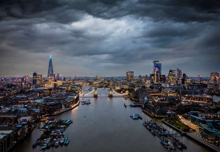 Elevated, moody view to the illuminated skyline of London, United Kingdom, with a cloudy sky during duskの写真素材