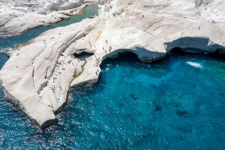 Aerial view of the chalk rock formations of Sarakiniko with people enjoying the sparkling blue sea on a hot summer day, Milos island, Cyclades, Greeceの写真素材