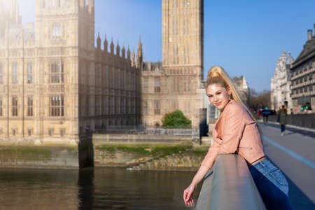 A beautiful tourist woman stands in front of the Big Ben tower at Westminster, London, during her city sightseeing tripの写真素材