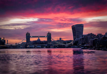 Low angle view over the Thames river to the skyline of the City of London and Tower Bridge during a colorful sunsetの写真素材