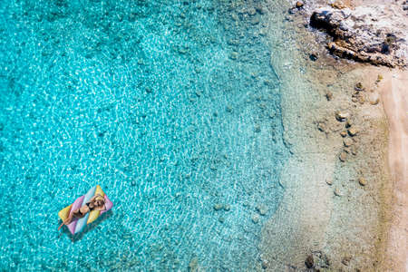 A woman in bikini on a float enjoys the turquoise waters of the Aegean Sea in Greece during summer timeの写真素材