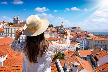 A tourist woman takes photos of the beautiful cityscape of Lisbon, with the colorful houses and roofs at the Alfama district, Portugalの写真素材