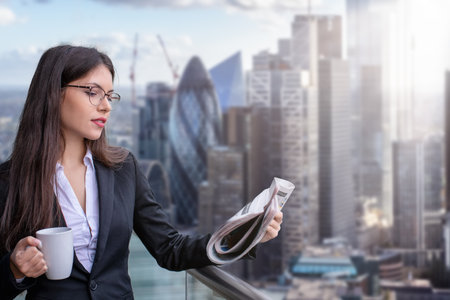 A attractive businesswoman in corporate outfit reading morning newspaper and holding a coffee cup in front of the City of London skylineの写真素材