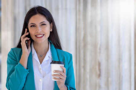 Portrait of a beautiful, young woman in a business outfit talking on her mobile phone and holding a coffee cupの写真素材