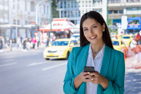 Portrait of a young, professional, Greek woman in corporate outfit holding her mobile phone in the city center of Athens, Greeceの写真素材