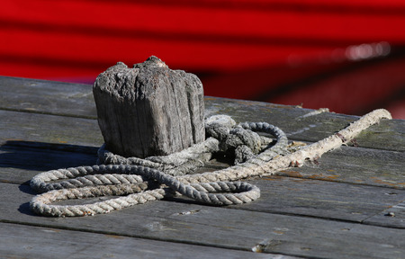 A bollard, a rope and a red fishing boat in the harbour, Grisslehamn, Sweden.