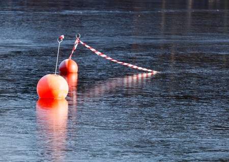 Two orange buoys reflecting in the thin iceの写真素材