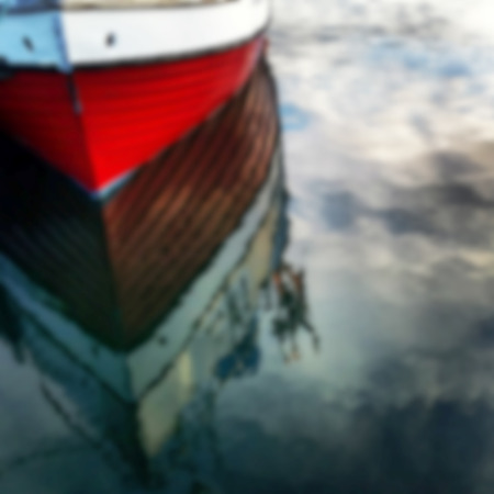 Defocused red boat reflecting in blue waterの写真素材