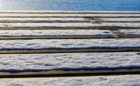 Low angle view of a bridge made of plank partly covered with snow and glimps of the oceanの写真素材