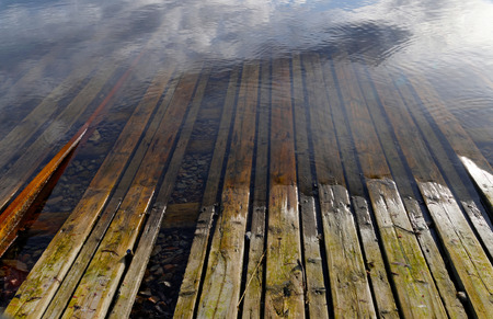 Wooden ramp used for putting boats into sea and the sky reflecting in the waterの写真素材