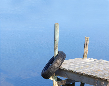 Silhouette of a tiny wooden bridge and a tyre. Calm blue water in the backgroundの写真素材