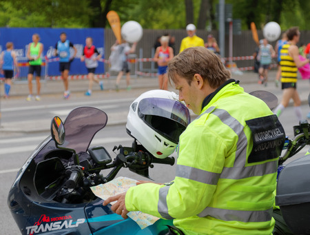 STOCKHOLM - MAY 30, 2015: Security man on motor cycle studying the map of the race track before the start of the ASICS Stockholm Marathon event May 30, 2015 in Stockholm, Sweden. People warming up in the backgroundのeditorial素材
