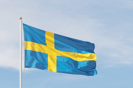 Swedish flag outside the Royal castle, blue and a yellow cross and background of blue sky and white cloudsの写真素材