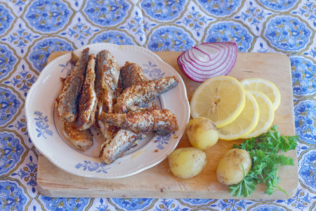 Swedish delicacy consisting of a plate of fried baltic herring, potato, red onion, lemon and parsley on a table with a blue textured clothの写真素材