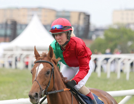 STOCKHOLM - JUNE 06: Female jockey in red, green and white clothes riding a horse race in the horse race at the Nationaldags Galoppen at Gardet. June 6, 2015 in Stockholmのeditorial素材