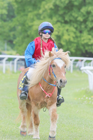 STOCKHOLM - JUNE 06, 2015: Young girl wearing sun glasses sitting on a brown pony at the Nationaldags Galoppen at Gardet. June 6, 2015 in Stockholmのeditorial素材