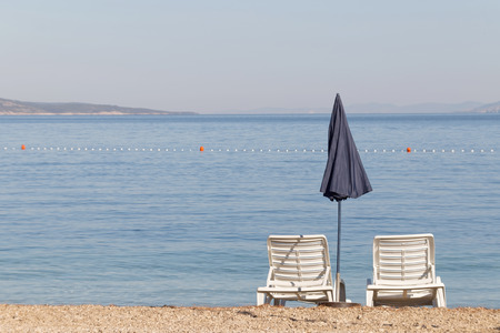 Two white empty deck chair and a blue parasol on the beach in the early morning before the tourists arriveの写真素材
