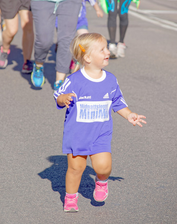 STOCKHOLM, SWEDEN - AUG 15, 2015: Young blonde girl smiling and running in the section for kids of age 2-7 years in the running event Midnattsloppet, August 15, 2015 in Stockholm, Swedenのeditorial素材