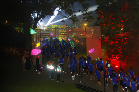 STOCKHOLM, SWEDEN - AUG 15, 2015: Group of runners in blue dresses running throgh a tunnel with a colorful laser show in the running event Midnattsloppet, August 15, 2015 in Stockholm, Swedenのeditorial素材