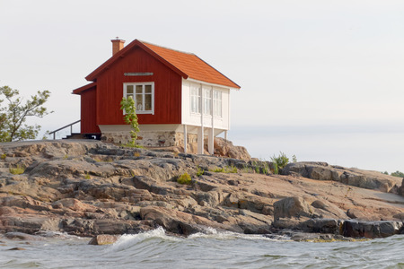 Red and white traditional cottage built on a rock in the archilelagoの写真素材