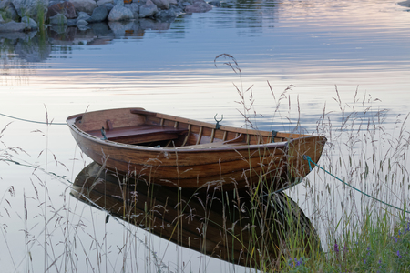 Wooden rowboat in the calm water in a small harbor in the evening light. Front side view. Grass in the foregroundの写真素材