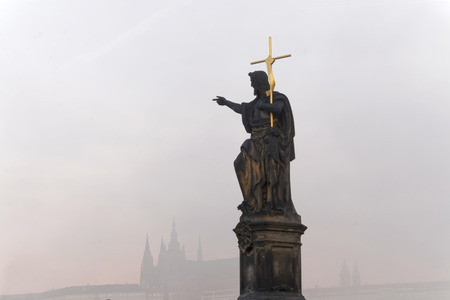 PRAGUE, CZECHOSLOVAKIA - DEC 07, 2015: Statue with a golden cross on Charles bridge in Prague. The royal castle in the background. December 07, 2015 in Prague, Czechoslovakiaのeditorial素材