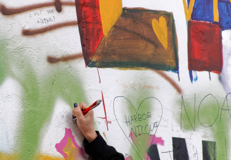 PRAGUE, CZECHIA - DEC 05, 2015: Female hand writes on the colorful public John Lennon Wall where there is a continous graffiti painting going on by tourists. December 05, 2015 in Prague, Czechiaのeditorial素材