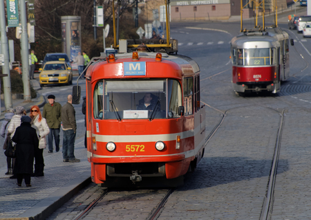 PRAGUE, CZECHIA - DEC 04, 2015: Two red and white vintage tram in evening light driving on a cobblestone street in the city. People waiting. December 04, 2015 in Prague, Czechiaのeditorial素材