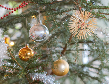 Christmas decorations hanging on a christmas tree branch. Colorful silver and blue balls and a star made of hay. Short depth of focusの写真素材