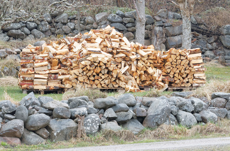 Large stack of birch firewood. Rural stone wall behind and in frontの写真素材