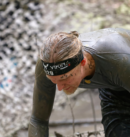 STOCKHOLM, SWEDEN - MAY 14, 2016: Man covered with mud crawling under a camouflage net in the...