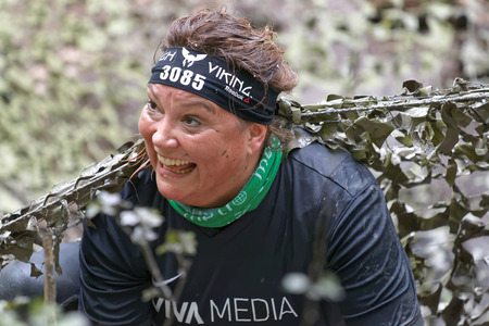 STOCKHOLM, SWEDEN - MAY 14, 2016: Smiling senior woman covered with mud crawling under a camouflage net in the obstacle race Tough Viking Event in Sweden, April 14, 2016のeditorial素材