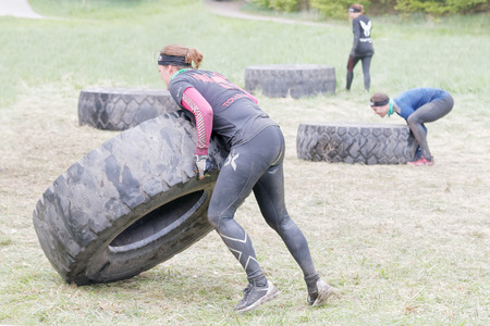 STOCKHOLM, SWEDEN - MAY 14, 2016: Man and woman struggling to tip a large tractor tire obstacle in the obstacle race Tough Viking Event in Sweden, April 14, 2016のeditorial素材