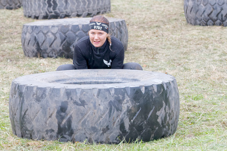 STOCKHOLM, SWEDEN - MAY 14, 2016: Woman struggling to tip a large tractor tire obstacle in the obstacle race Tough Viking Event in Sweden, April 14, 2016のeditorial素材