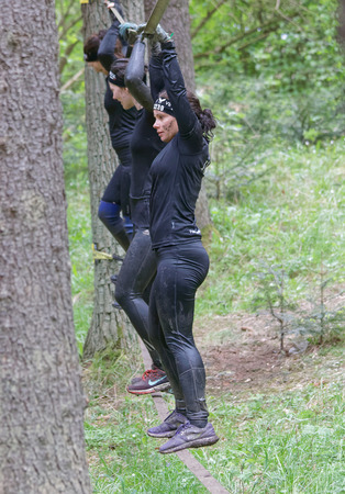 STOCKHOLM, SWEDEN - MAY 14, 2016: Side view of three woman with mud in their face trying to maintain the balance on a slack rope in the obstacle race Tough Viking Event in Sweden, April 14, 2016のeditorial素材