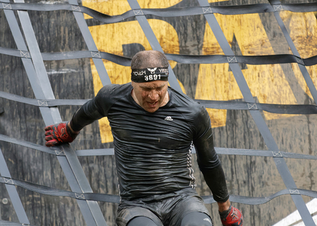 STOCKHOLM, SWEDEN - MAY 14, 2016: Man covered with mud climbing a net obstacle in the obstacle race...