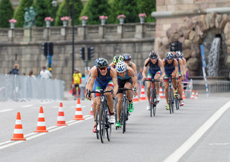 STOCKHOLM, SWEDEN - JUL 02, 2016: Group of colorful male triathlete cyclists, Gregory Barnaby (ITA), and competitors, the royal castle in background in the Men's ITU World Triathlon series event July 02, 2016 in Stockholm, Swedenのeditorial素材