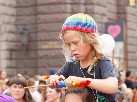 STOCKHOLM, SWEDEN - JUL 30, 2016: Blonde little boy wearing a rainbow hat, fixing the rainbow flag sitting on his mothers shoulders in the Pride parade July 30, 2016 in Stockholm, Swedenのeditorial素材