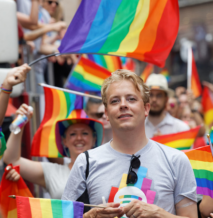 STOCKHOLM, SWEDEN - JUL 30, 2016: Smiling blonde man, lots of rainbow Pride flags in the background in the Pride parade July 30, 2016 in Stockholm, Swedenのeditorial素材