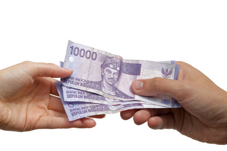 Paying - hand giving Indonesian rupiah banknotes to another handの写真素材