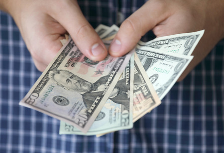 Hands holding US dollar bank notes, a blue shirt in the background. Short depth of focusの写真素材