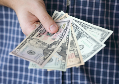 Hand holding US dollar bank notes, a blue shirt in the background. Short depth of focusの写真素材