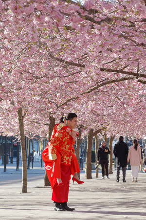 STOCKHOLM, SWEDEN - APRIL 23, 2016: Asian couple in traditional red and golden clothes in the beautiful park Kungstradgarden full of pink cherry bloom.
The man lifting the woman up on his backのeditorial素材