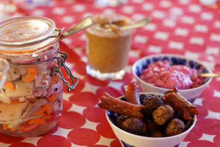Home made pickled herring, onion and carrot in a glass jar, meatballs, sausage, beetroot salad and mustard on the Christmas table with a red cloth
の写真素材