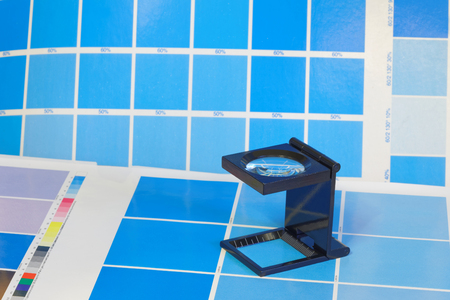 Magnifying glass standing on a leaf of the cyan test print in a pre-press workshop. Very short depth of focusの写真素材