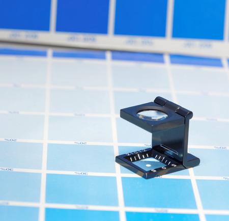 Magnifier or printer's loupe sits on a cyan test sheet in a pre-press workshopの写真素材