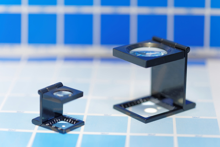 Two magnifier or printer's loupe sits on a cyan test sheet in a pre-press workshop. Very short depth of focusの写真素材