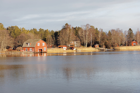 Old red boat house and other buildings in the swedish archipelago reflecting in the sea in the warm morning lightの写真素材